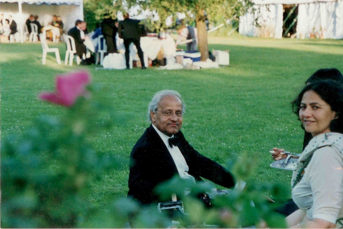 Sanjaya Lall in black tie, seated on a lawn at a summer party